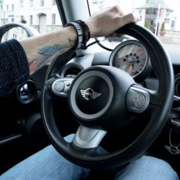 A person with tattoo holding the steering wheel